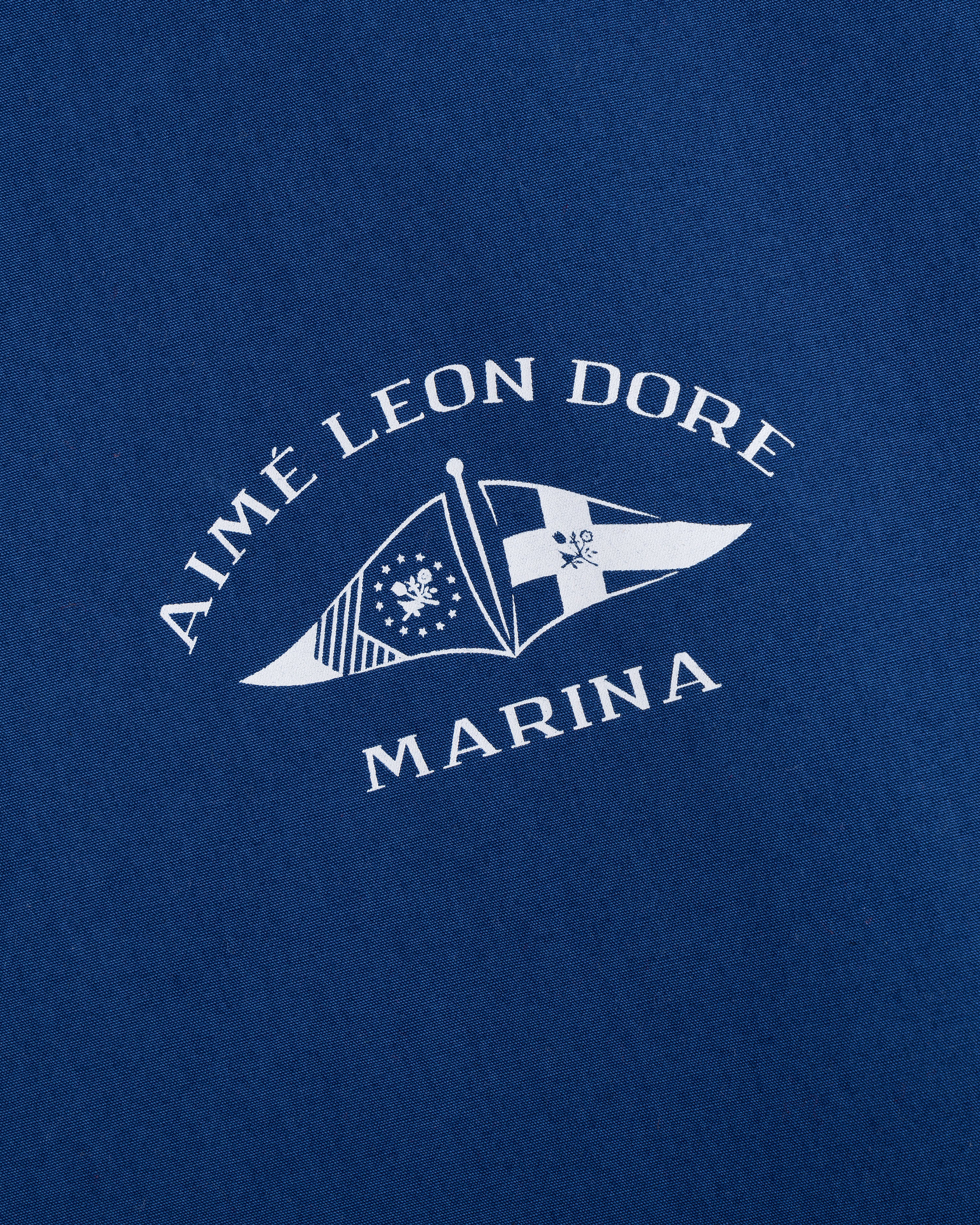 White Aimé Leon Dore Marina text and nautical flag logos printed on blue Marina Jacket fabric.