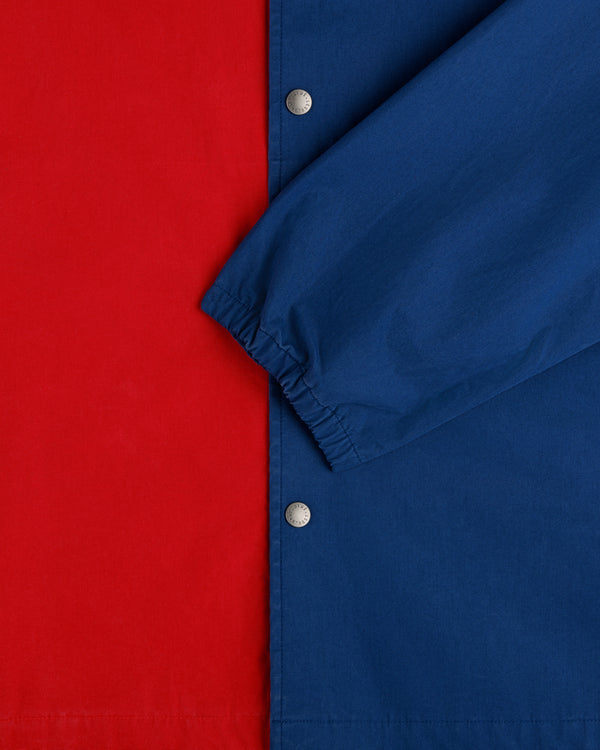 Close-up of the Marina Jacket featuring a red body, blue sleeve, silver snap buttons, and elastic wrist cuff.