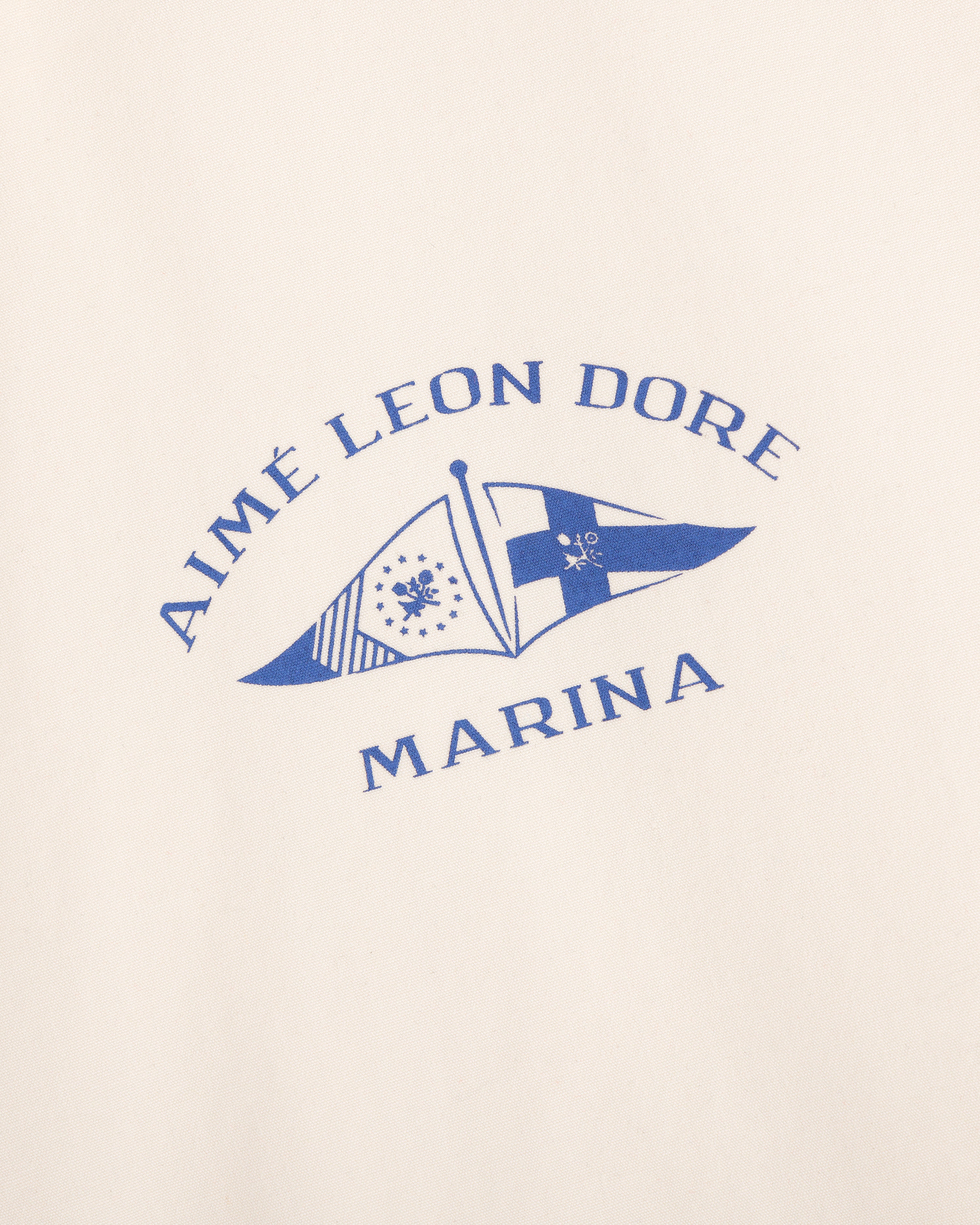 The Marina Jacket features blue Aimé Leon Dore Marina text and two nautical flags on a cream background.