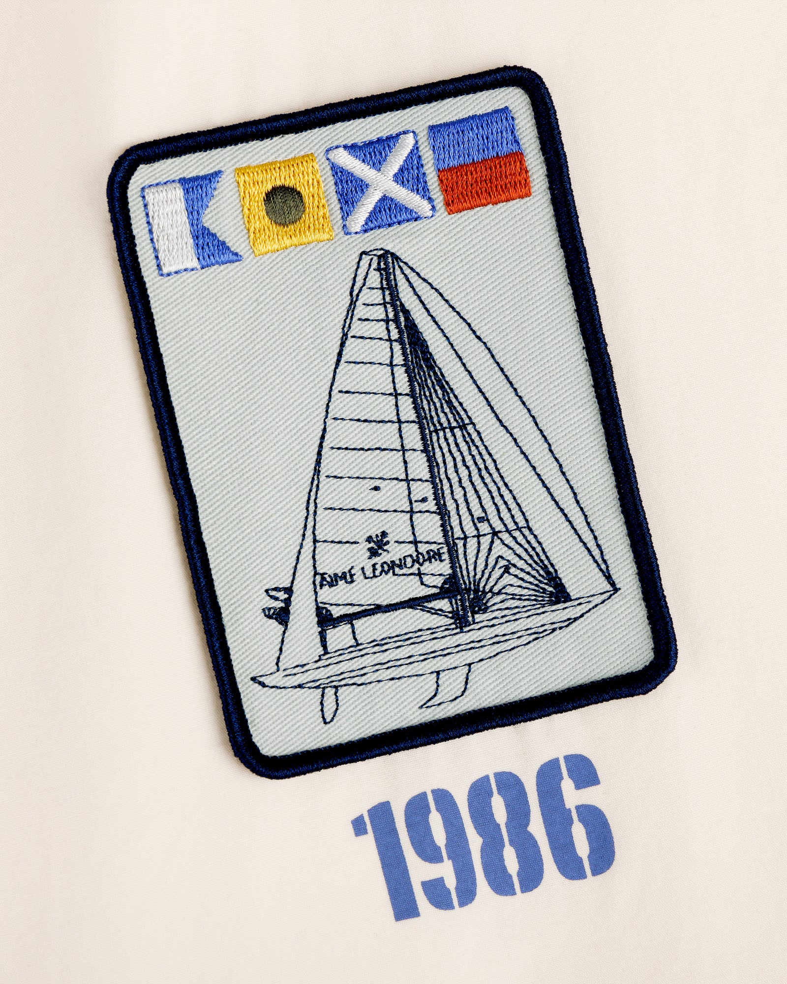 Embroidered Marina Jacket patch with sailboat, nautical flags, and "1986" below.