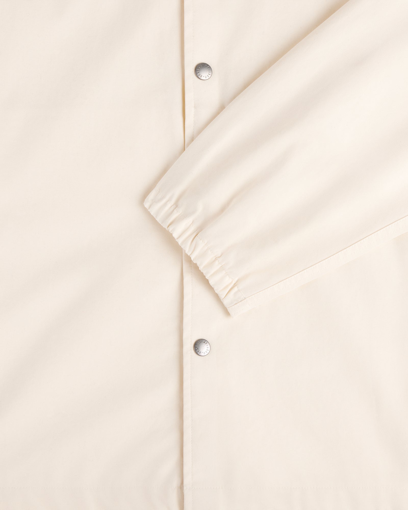 Close-up of the Marina Jacket in cream with silver snap buttons and an elastic cuff on one sleeve.