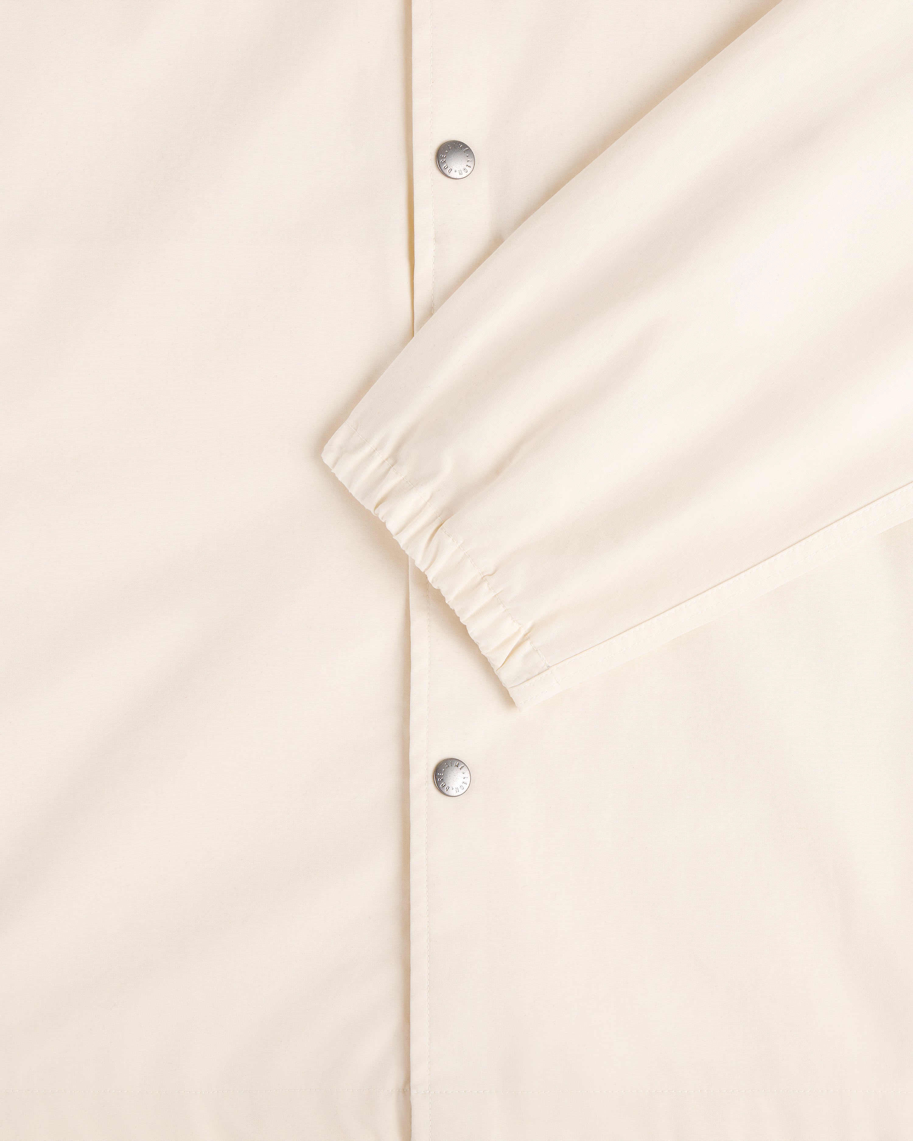 Close-up of the Marina Jacket in cream with silver snap buttons and an elastic cuff on one sleeve.
