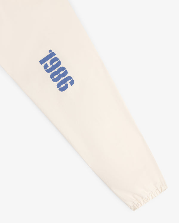 Marina Jacket: Beige sleeve with blue "1986" printed vertically near the wrist and an elastic cuff.
