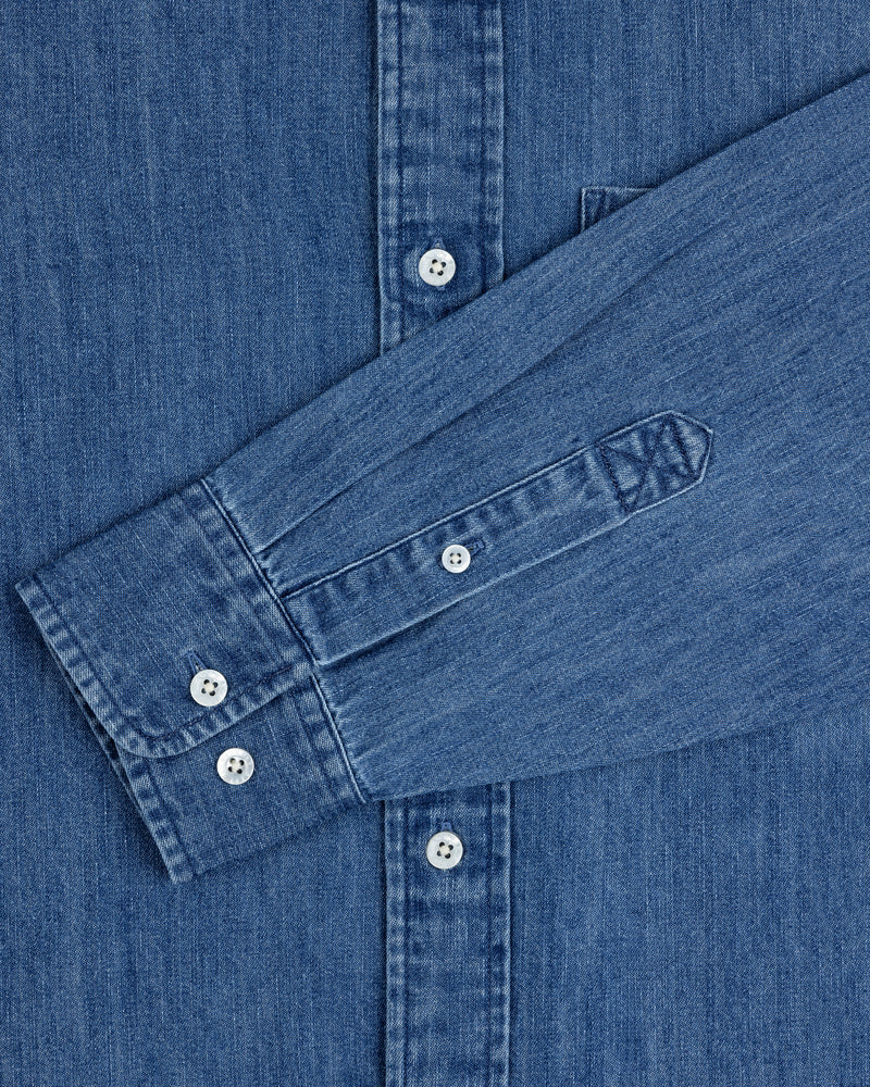Crest Chambray Shirt with white buttons and long sleeves folded across the front.