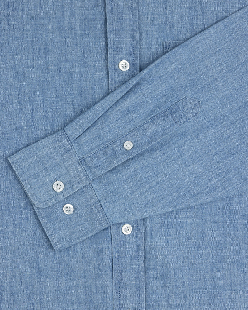 Crest Chambray Shirt in light blue, long sleeve with white buttons, shown flat with one sleeve folded across front.