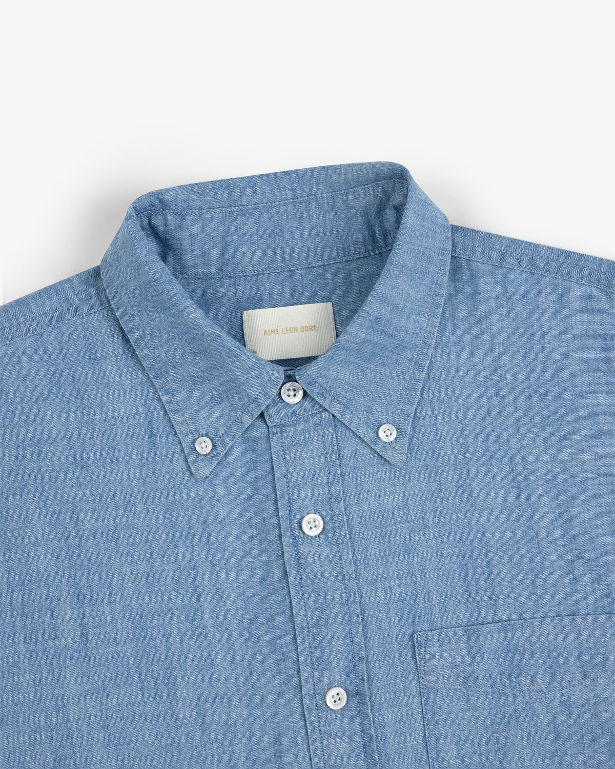Crest Chambray Shirt in light blue, button-up with collar and chest pocket, laid flat on white background.
