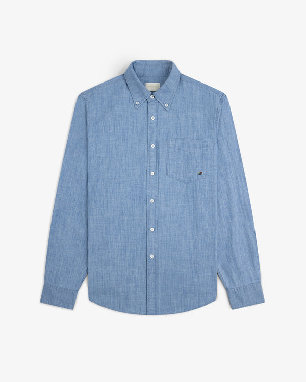 Crest Chambray Shirt in light blue with long sleeves and chest pocket, laid flat on a white background.