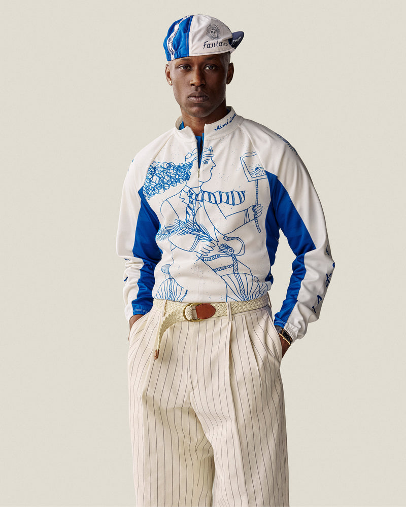 Man wearing Fassianos Cycling Cap, illustrated top, and cream pinstripe pants with hands in pockets.