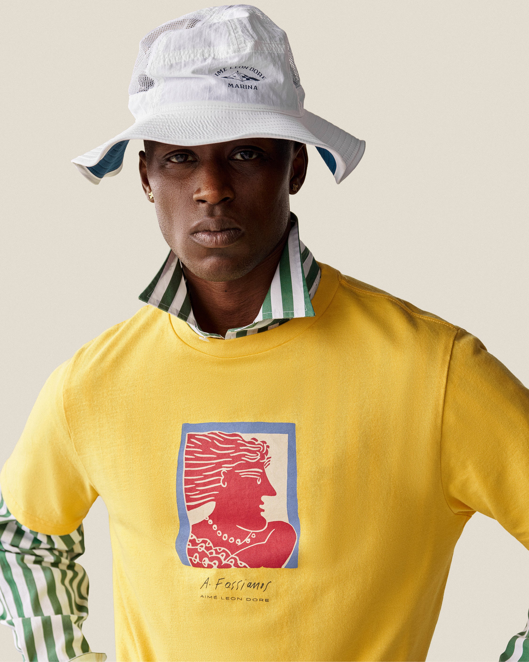 Man in a yellow graphic tee, green striped shirt, and Marina Boonie Bucket Hat poses against a plain background.