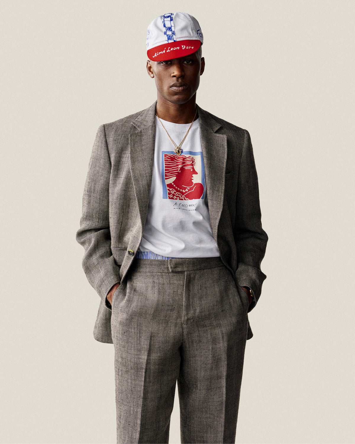 A man in Yarn Dyed Linen Suit Trousers, a white graphic tee, and cap stands with hands in pockets.