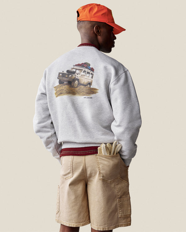 A man wears the Safari Crewneck Sweatshirt, tan shorts, and an orange cap, standing with his back turned.