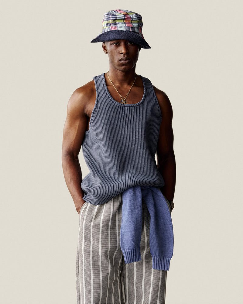 Man in a Stone Washed Knit Tank Top, striped pants, bucket hat, and sweater tied at waist stands against plain background.