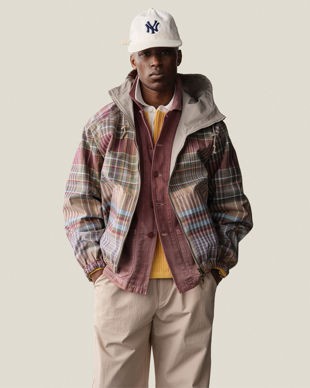 A man in a Reversible Madras Windbreaker, yellow sweater, tan pants, and NY cap stands facing forward.
