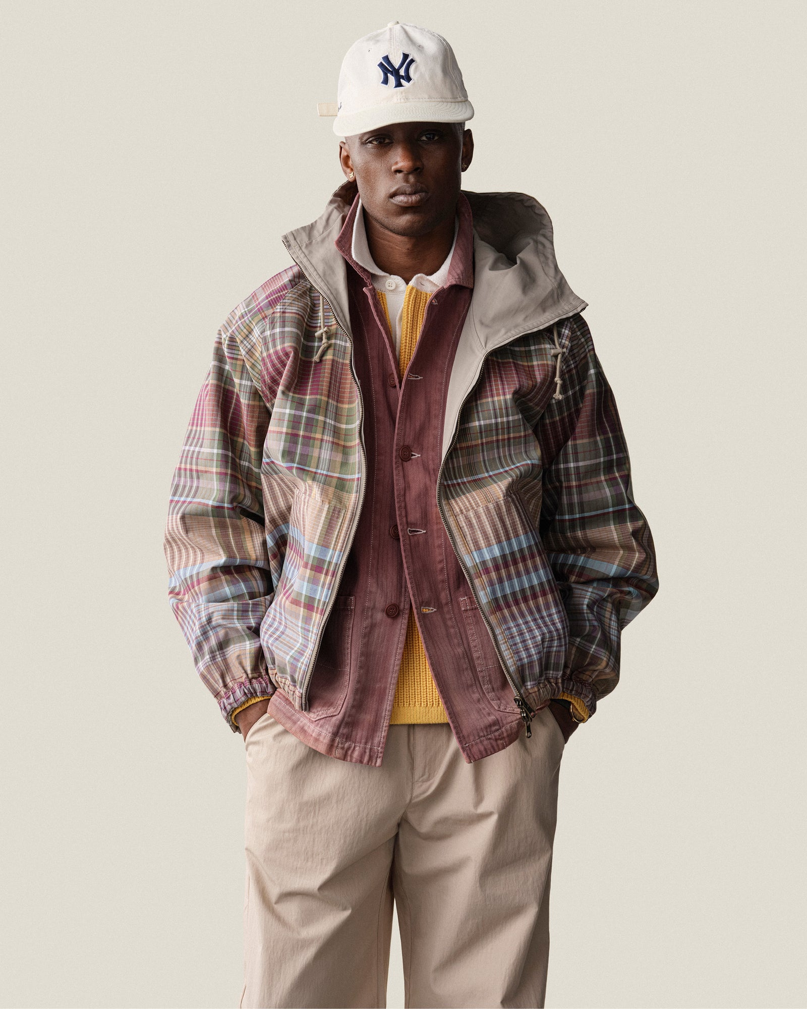 A man in a Reversible Madras Windbreaker, yellow sweater, tan pants, and NY cap stands facing forward.