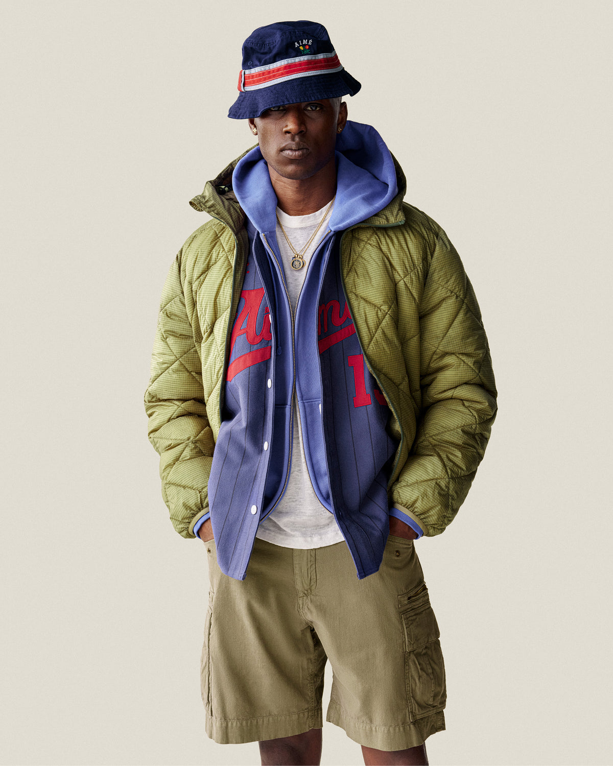 Man wearing a Sun Faded Full-Zip Hoodie, blue bucket hat, layered jackets, and khaki cargo shorts against a plain background.