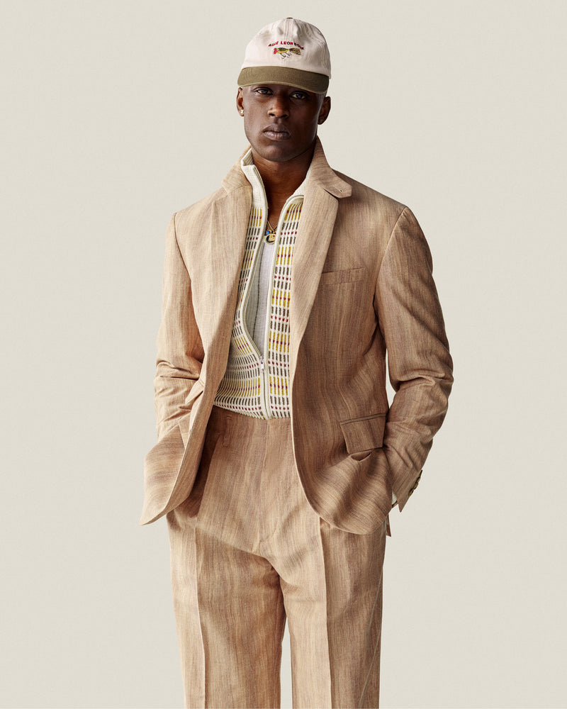 Man wears Multi Color Knit Track Sweater and beige cap, hands in pockets, standing against a plain background.