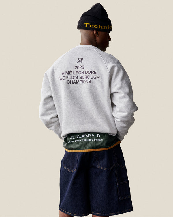 A person in the ALD / Technics World Champions Crewneck, beanie, and denim shorts stands facing away.