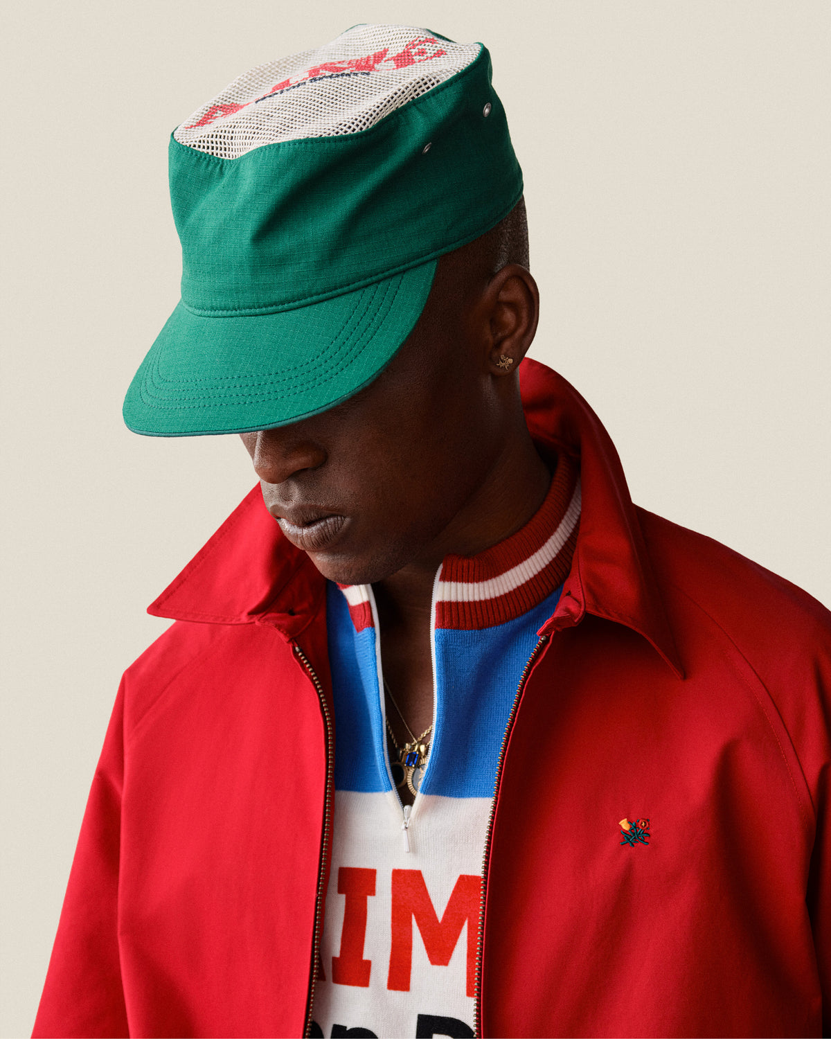 Person in an Aimé Painters Hat, red jacket, and colorful shirt looking down against a plain background.