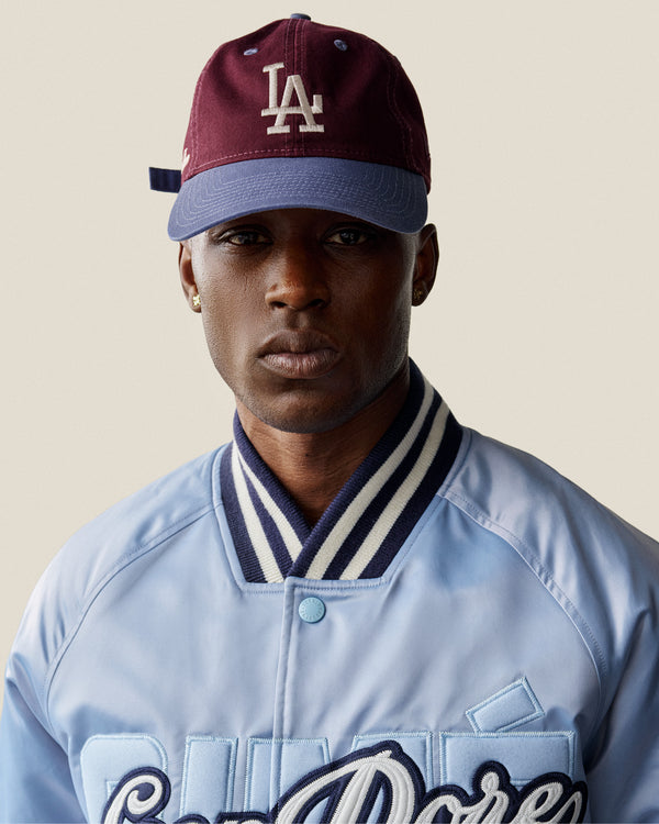 A person wearing the ALD / LA Dodgers Colorblock Ballpark Hat and a light blue jacket with dark stripes, facing the camera.