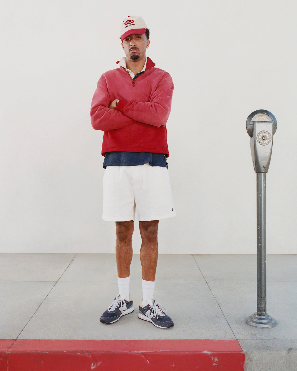 A man in a Sun Faded Crest Quarter Zip stands arms crossed beside a parking meter on the sidewalk.