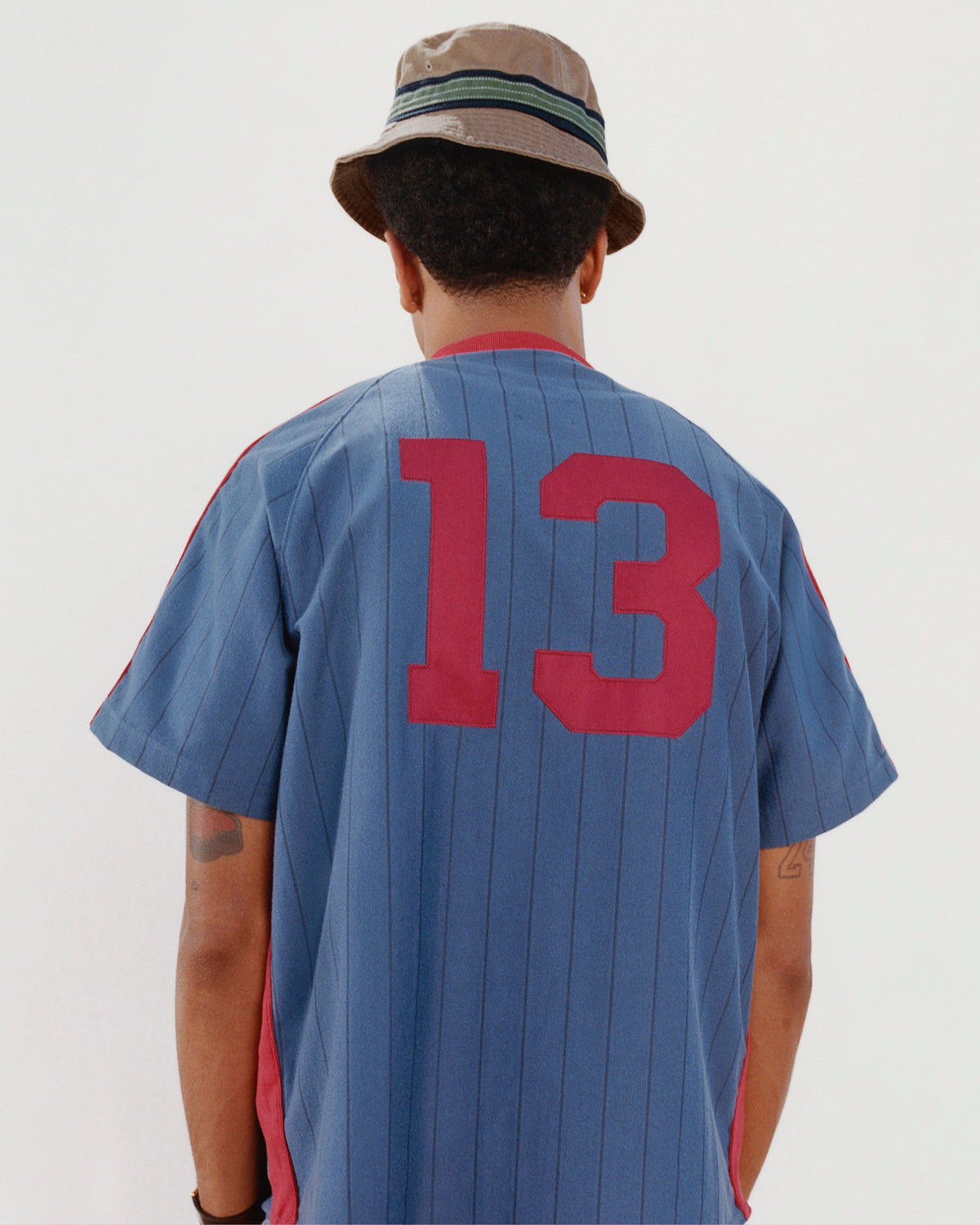 Person facing away, wearing a Crest Bucket Hat and a blue sports jersey with red number 13.
