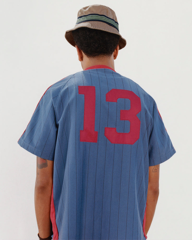 Person facing away, wearing a Crest Bucket Hat and a blue sports jersey with red number 13.