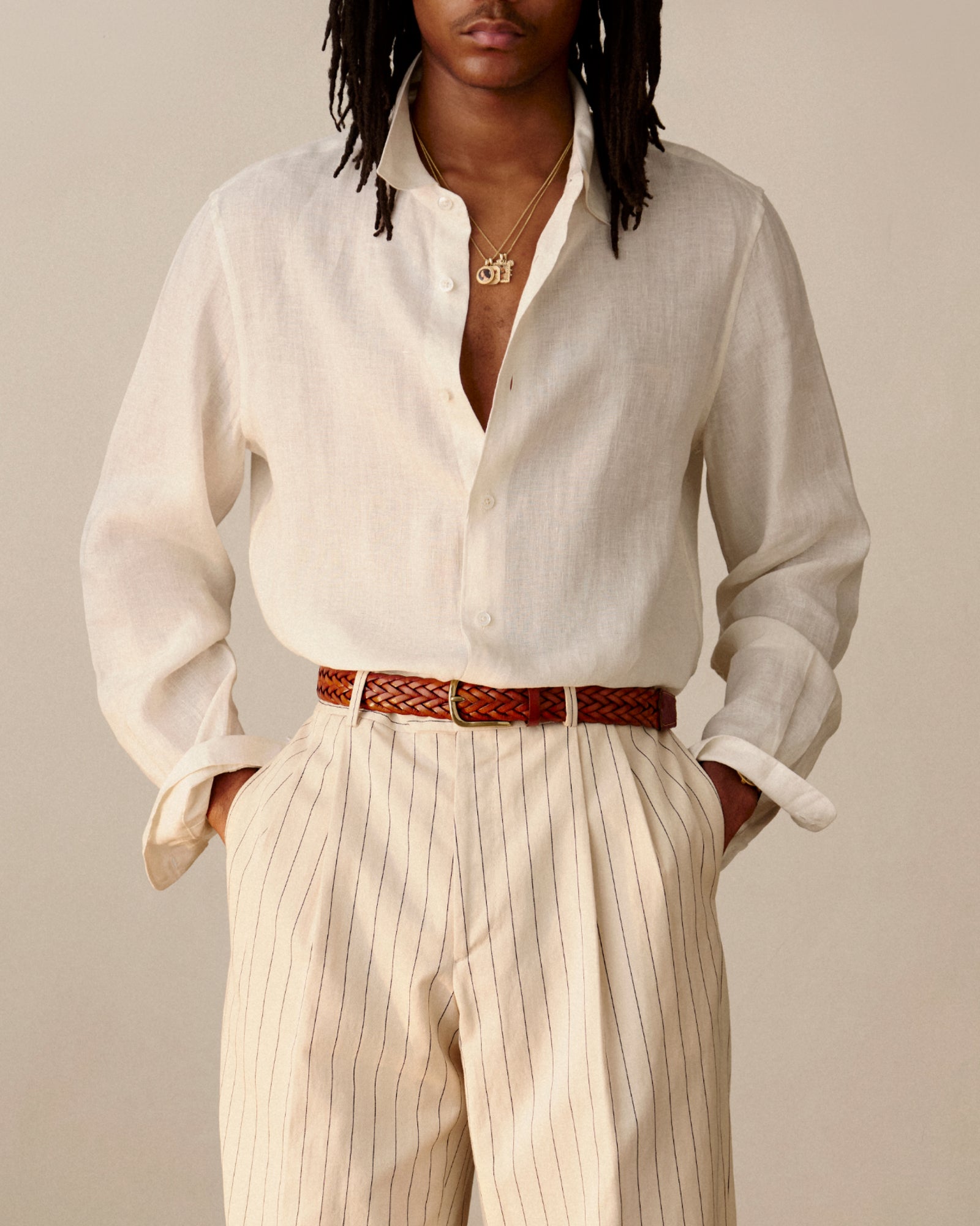 Someone in a Long-Sleeve Linen Shirt, pleated striped trousers, brown belt, and gold necklace.