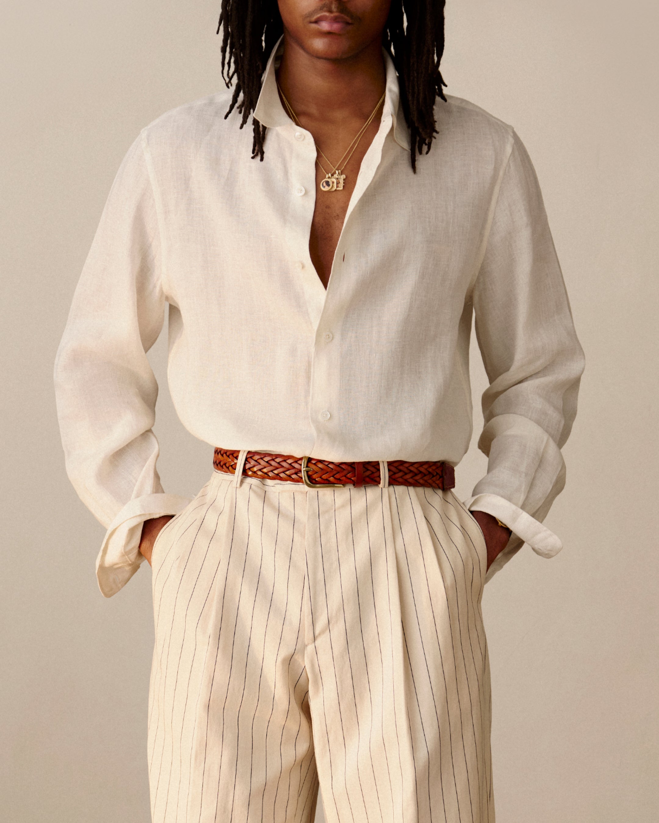 Someone in a Long-Sleeve Linen Shirt, pleated striped trousers, brown belt, and gold necklace.