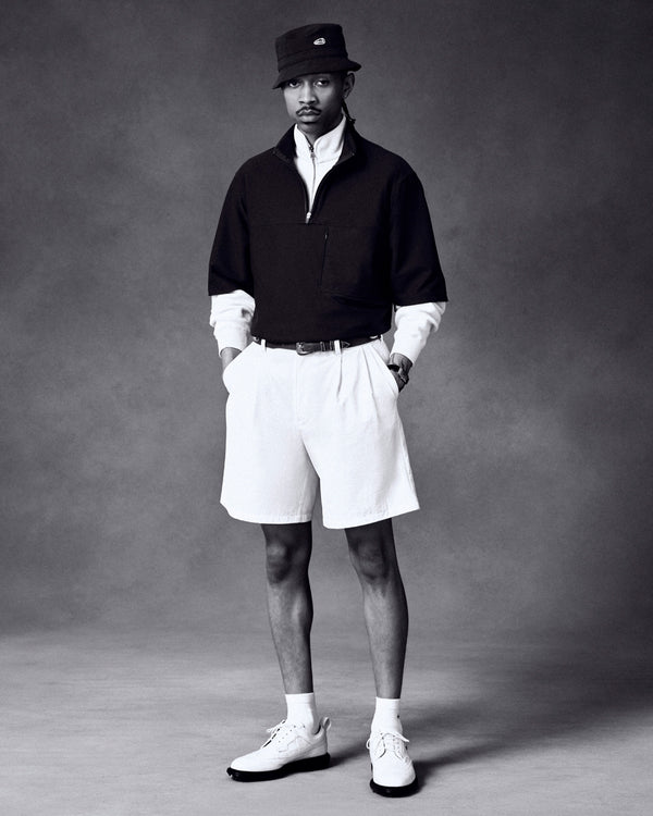 Man wearing ALD / Footjoy Croc-Embossed Premiere Series Marquis shoes, bucket hat, pullover, white shirt, and shorts in studio.