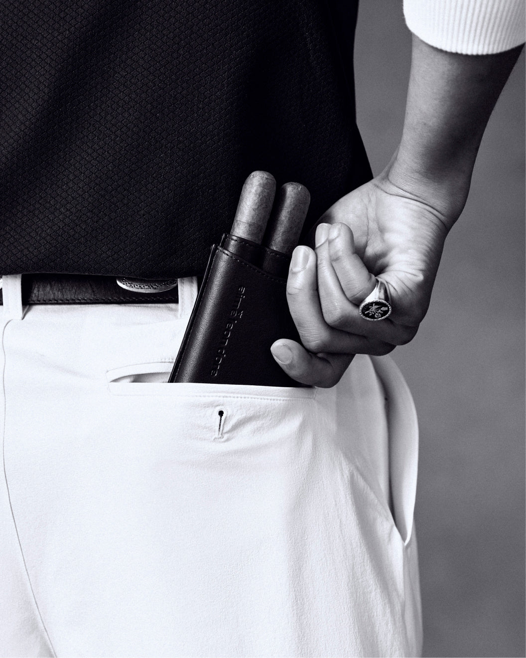 A person puts an ALD Golf Leather Cigar Case holding two cigars into the pocket of white pants, wearing a ring.