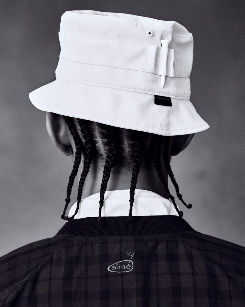 Person with braids wears the ALD Golf Bucket Hat and a dark checkered jacket, seen from behind against a neutral background.