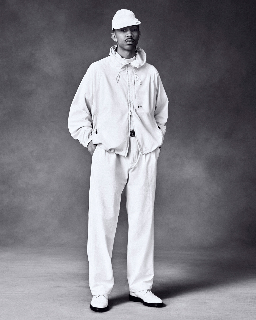 A man poses in the ALD Golf Lightweight Tips Windbreaker against a dark, textured studio background.