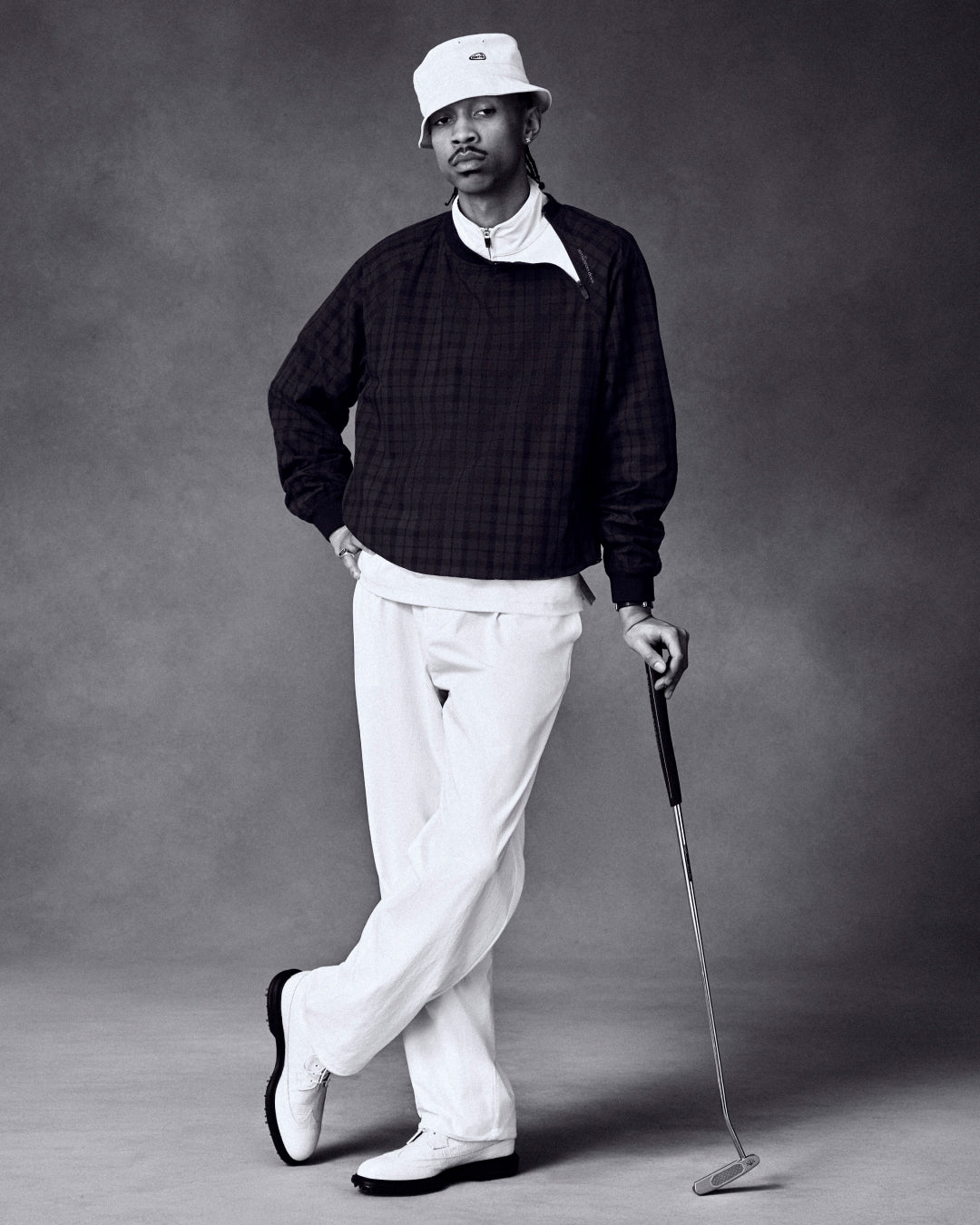Man wears ALD Golf Cordura Double Pleated Pant and poses with a golf club against a plain studio backdrop.