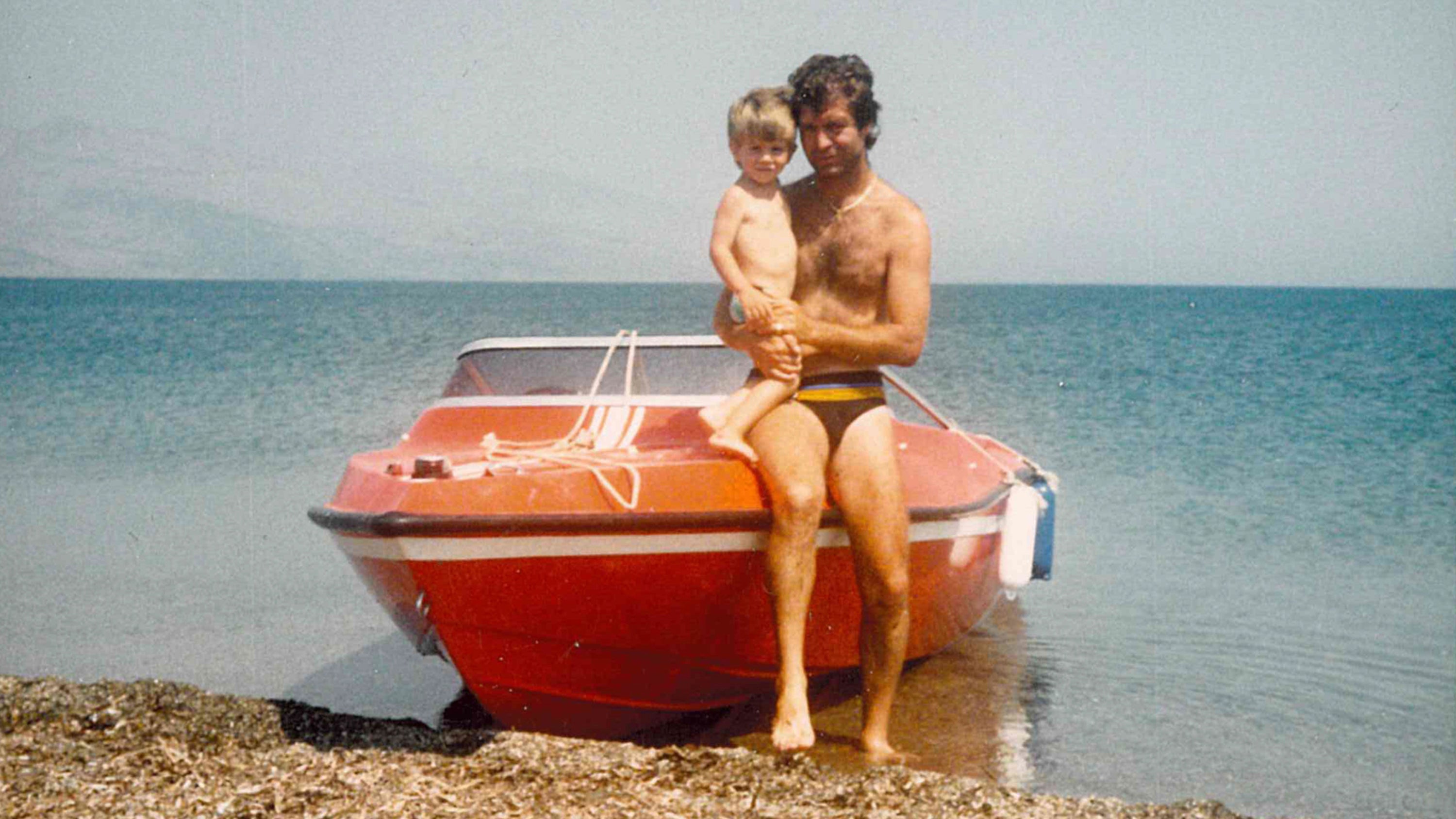 Man and child sitting on a red boat by the water
