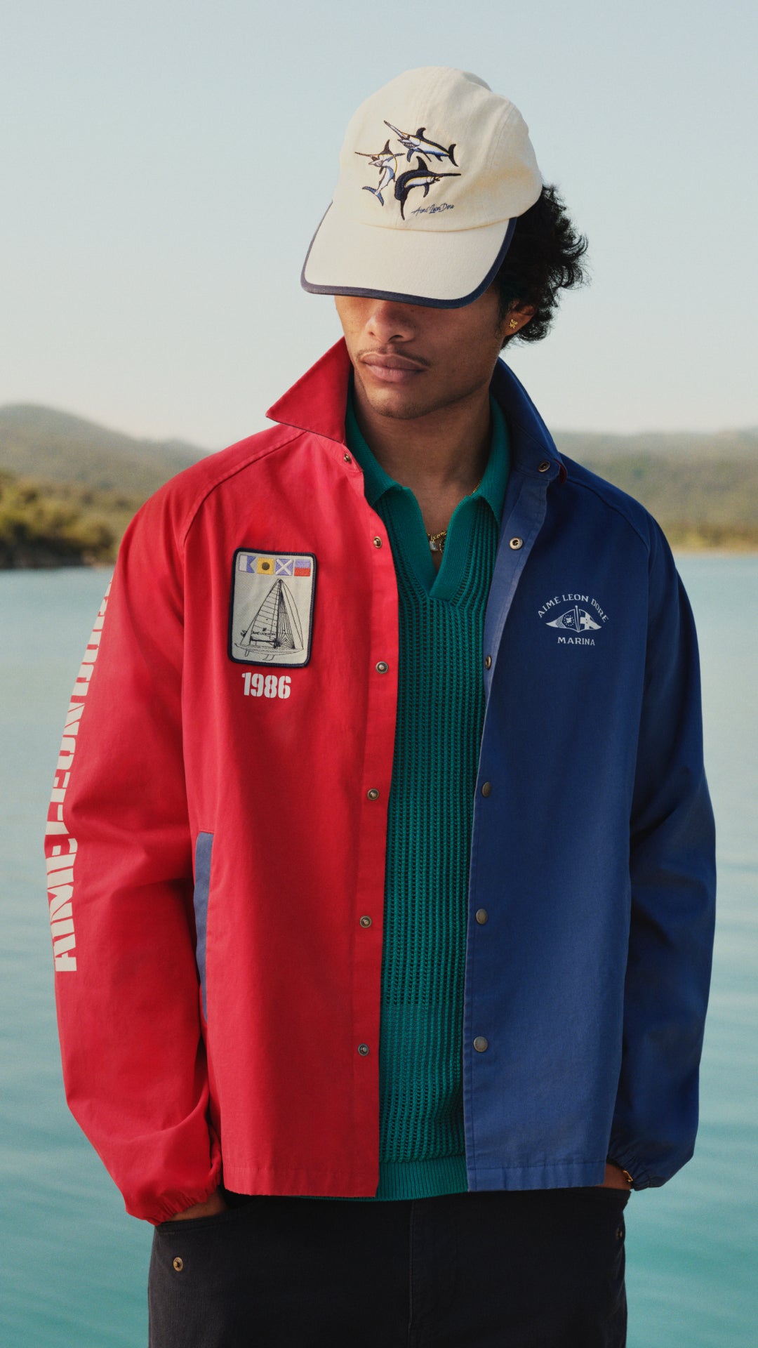 man wearing white cap covering face and blue and red jacket with water background
