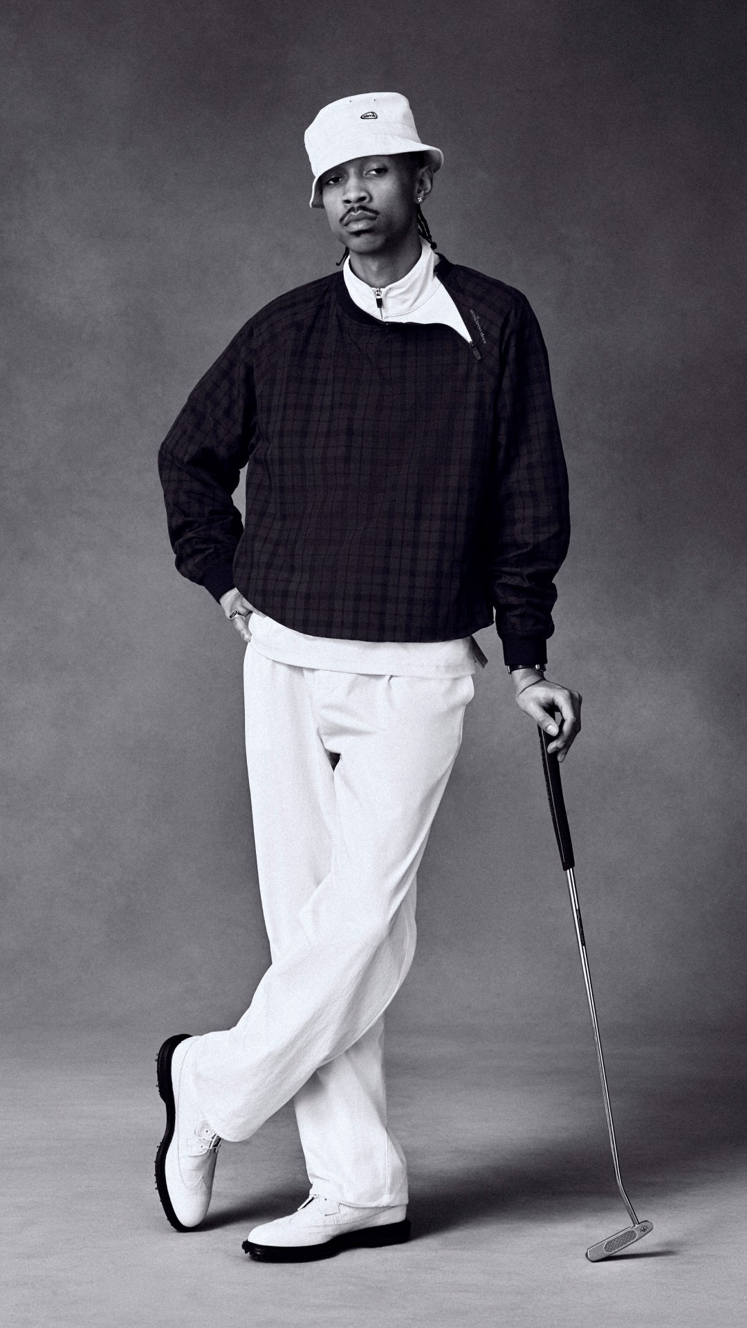 Man in golf attire holding a club against a gray background