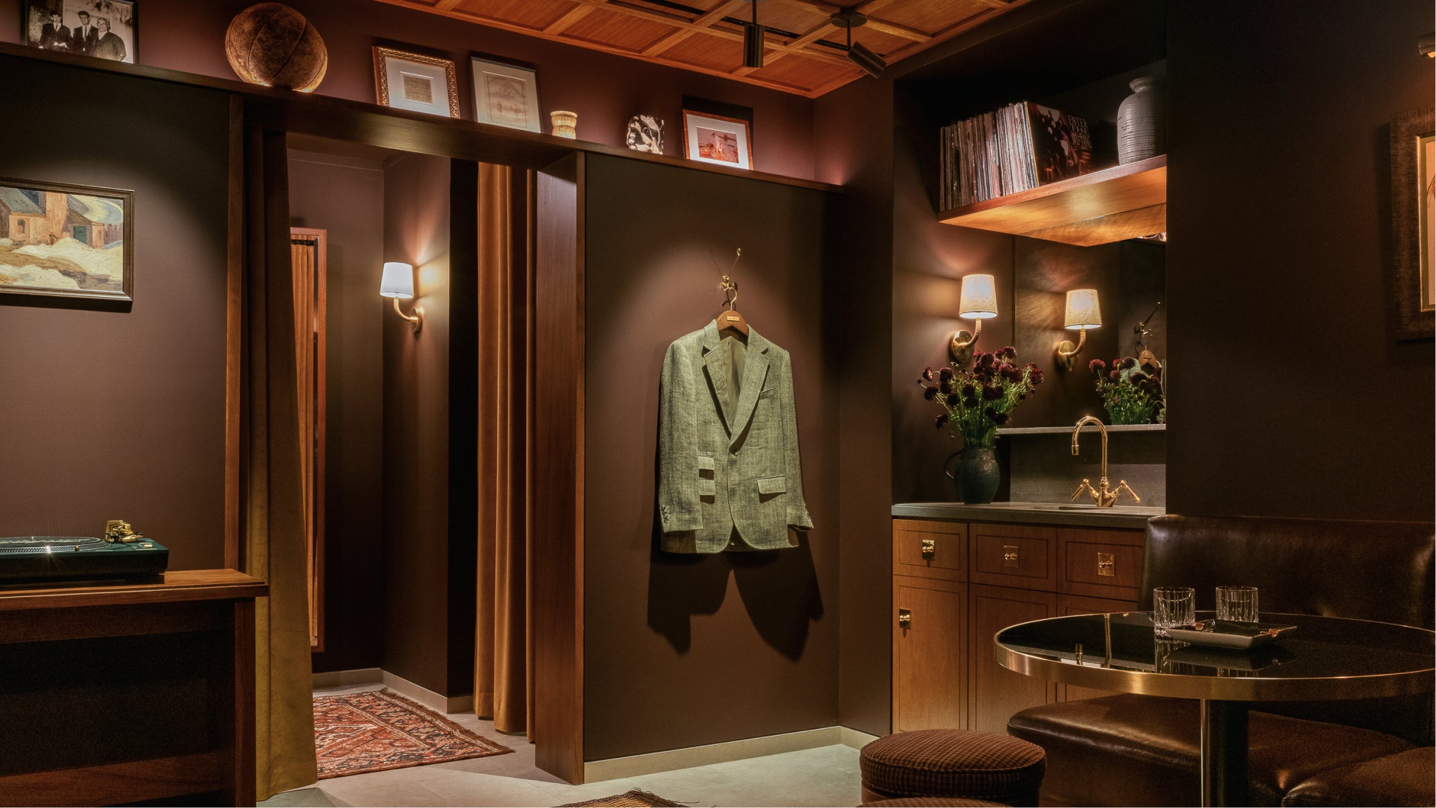 Green suit jacket hanging on a rack in a dimly lit room with a table and decor.