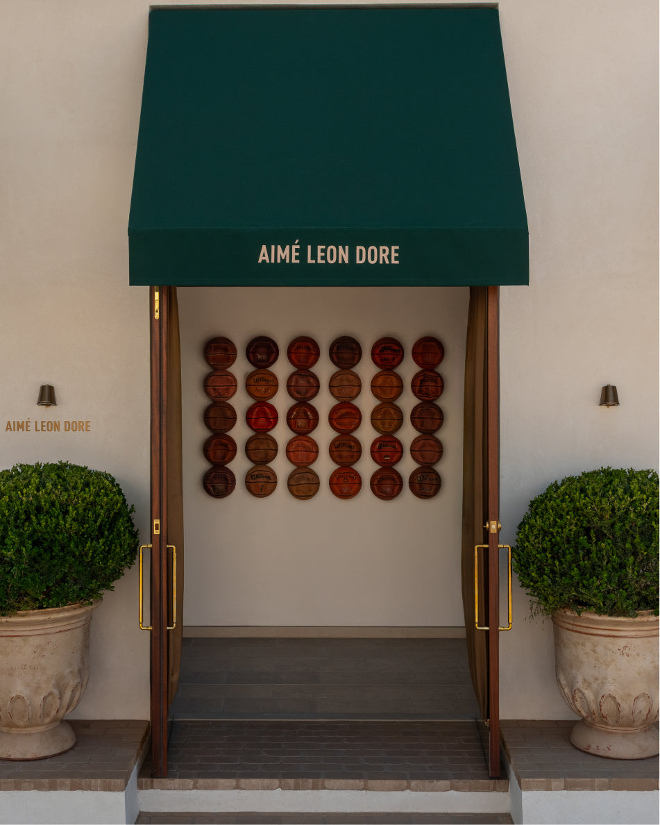 Aime Leon Dore store entrance with green awning and decorative wall.