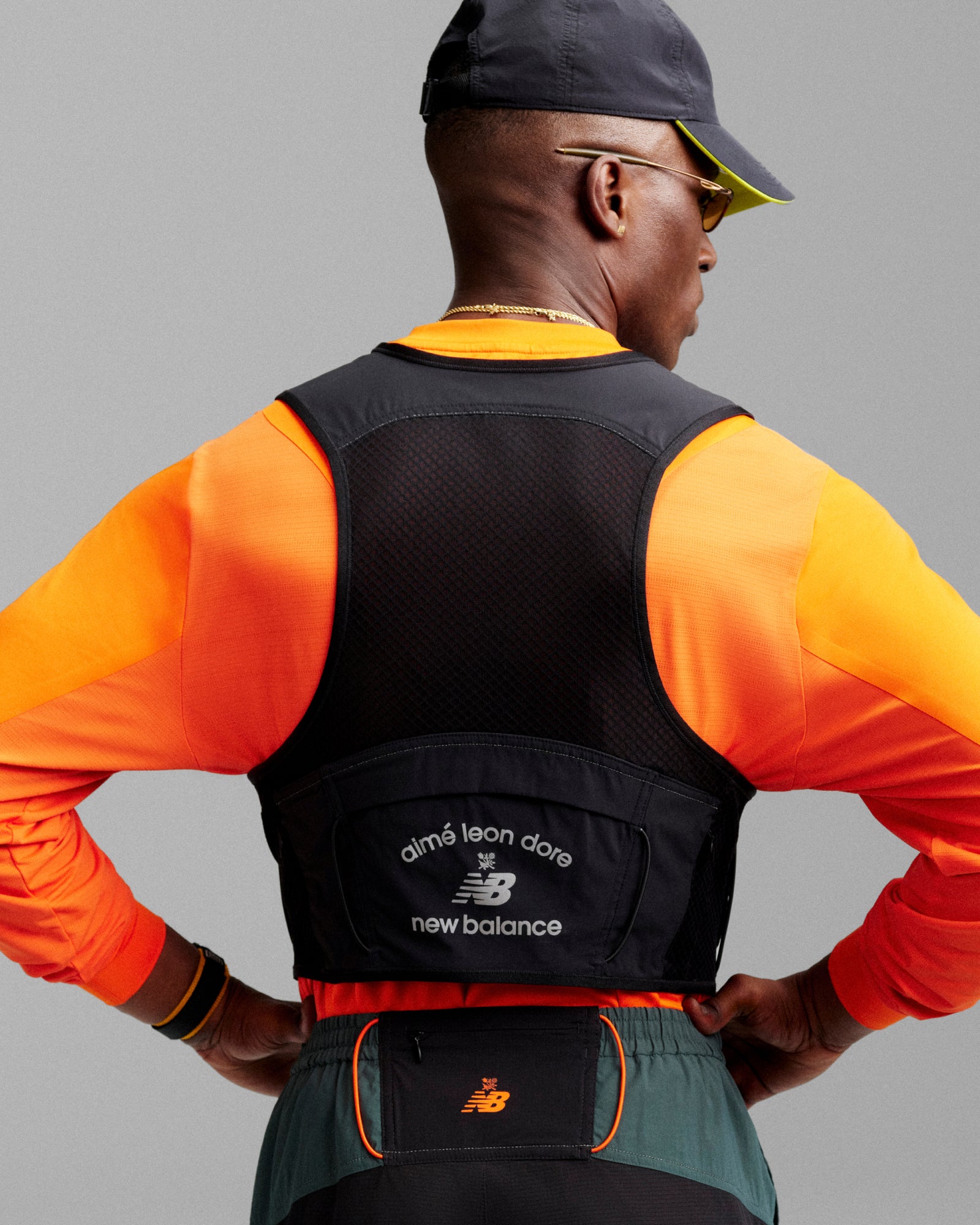 A man in orange athletic wear and a cap shows off the back of his black ALD / New Balance Hydrovest.