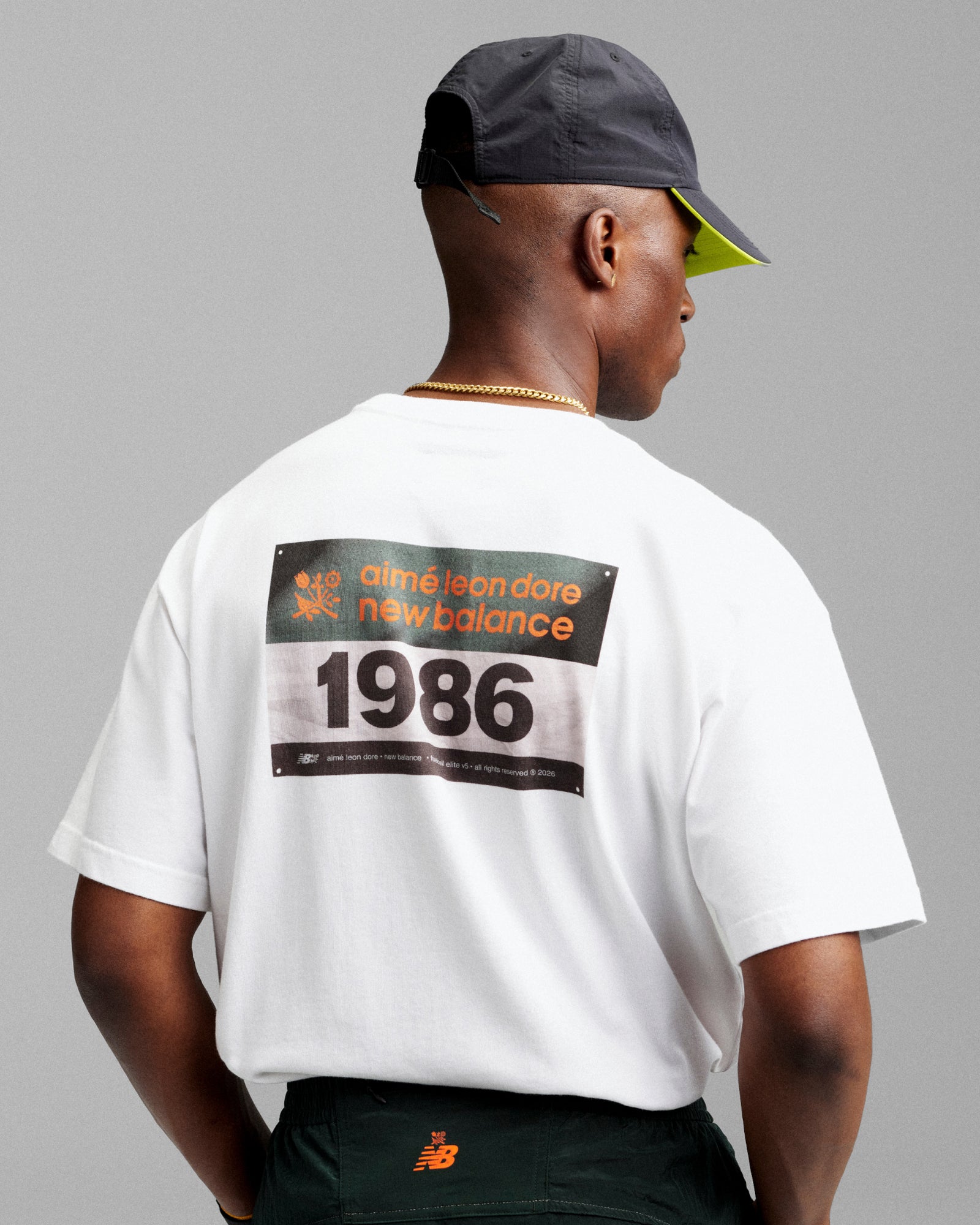 Man wearing a white ALD / New Balance Running Bib Tee with 1986 on the back and a black cap, facing away.