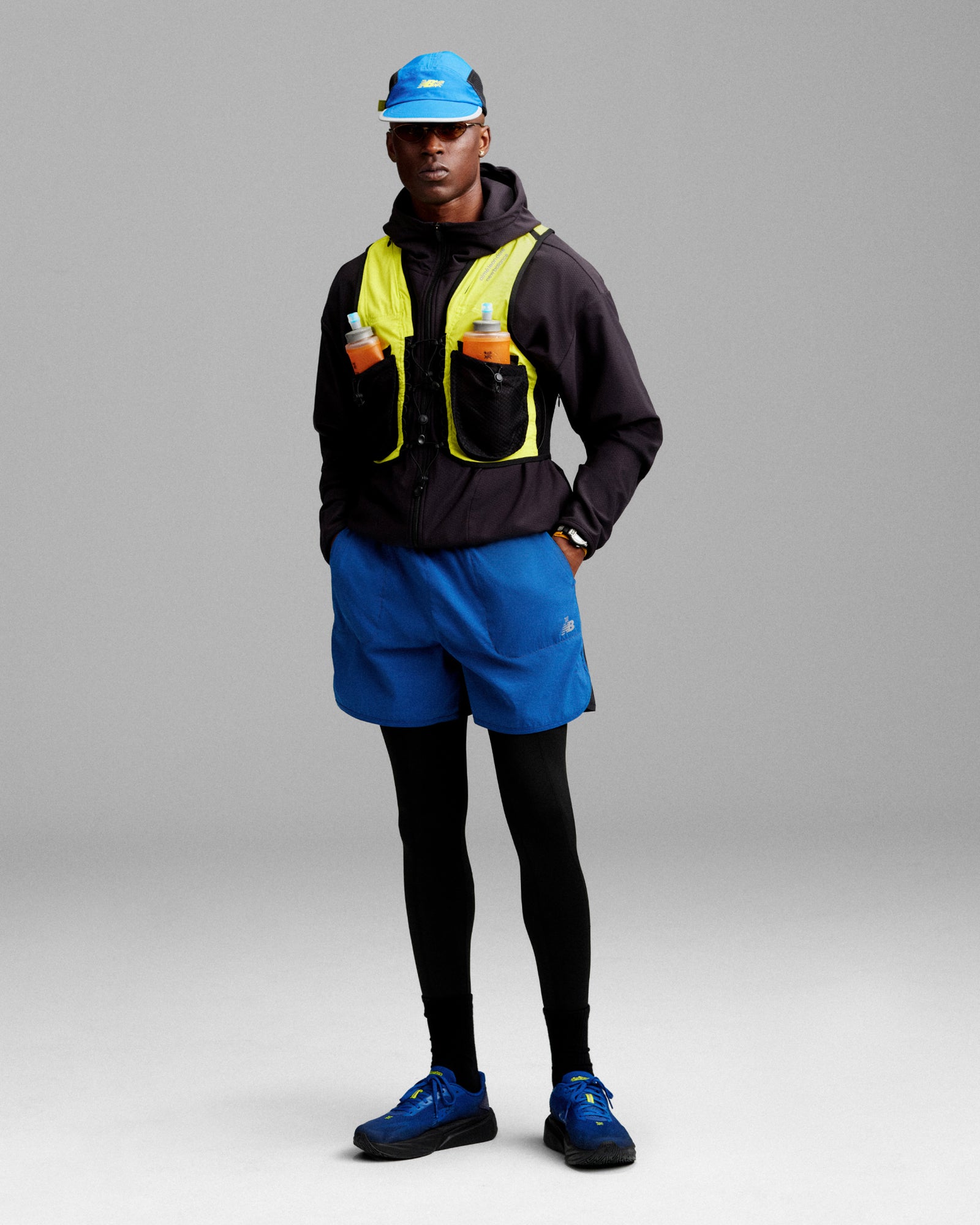 A person wears the ALD / New Balance Hydrovest over blue running gear and black tights, standing against a plain background.