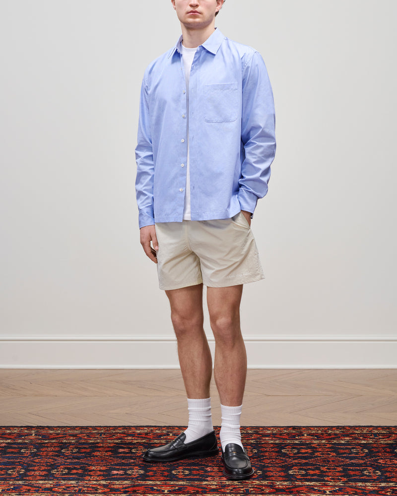 A person in a Poplin Casual Shirt, beige shorts, white socks, and black loafers stands on a patterned rug.
