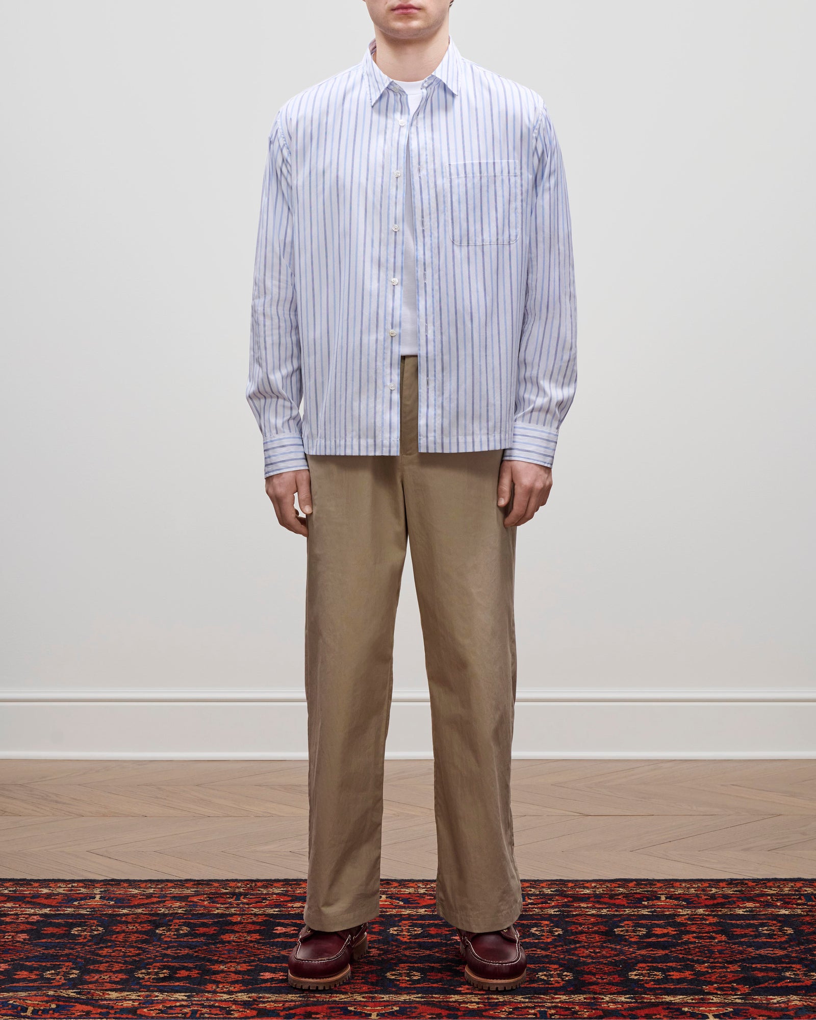 A person wears a Poplin Casual Shirt with tan pants and brown shoes, standing on a patterned rug.