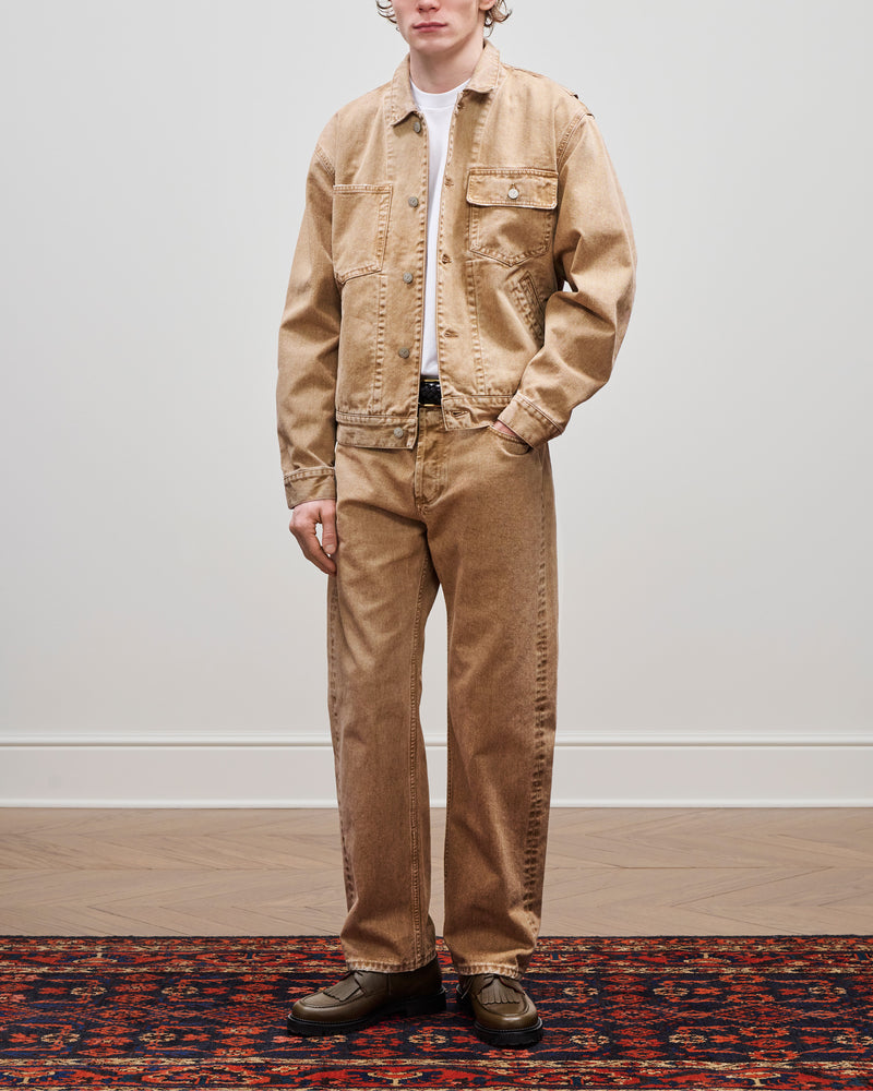 Person stands on a patterned rug, wearing a beige Denim Trucker Jacket, matching pants, and olive green shoes.