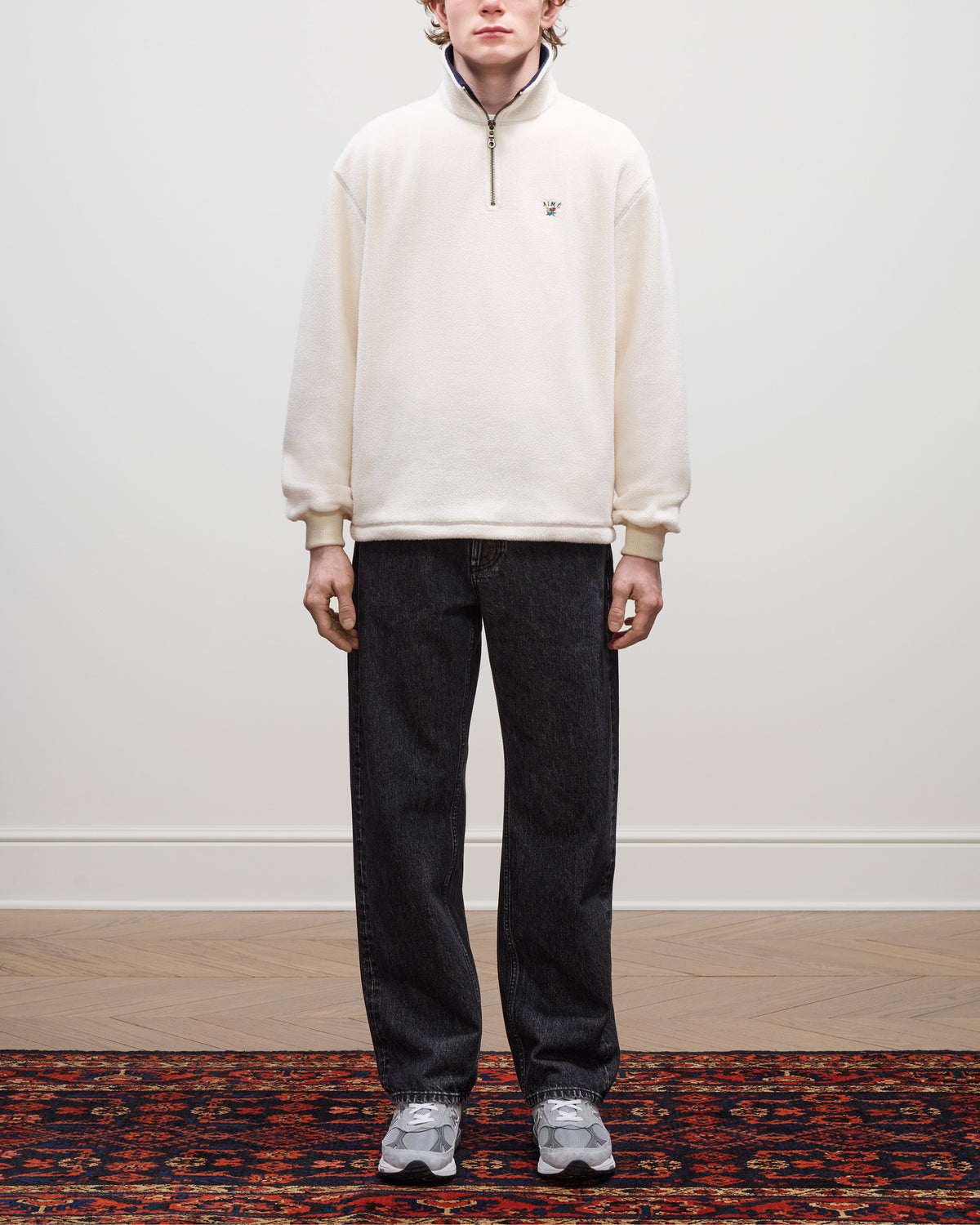 Person standing on a patterned rug, wearing a Crest Quarter-Zip Fleece Pullover, dark jeans, and gray sneakers.