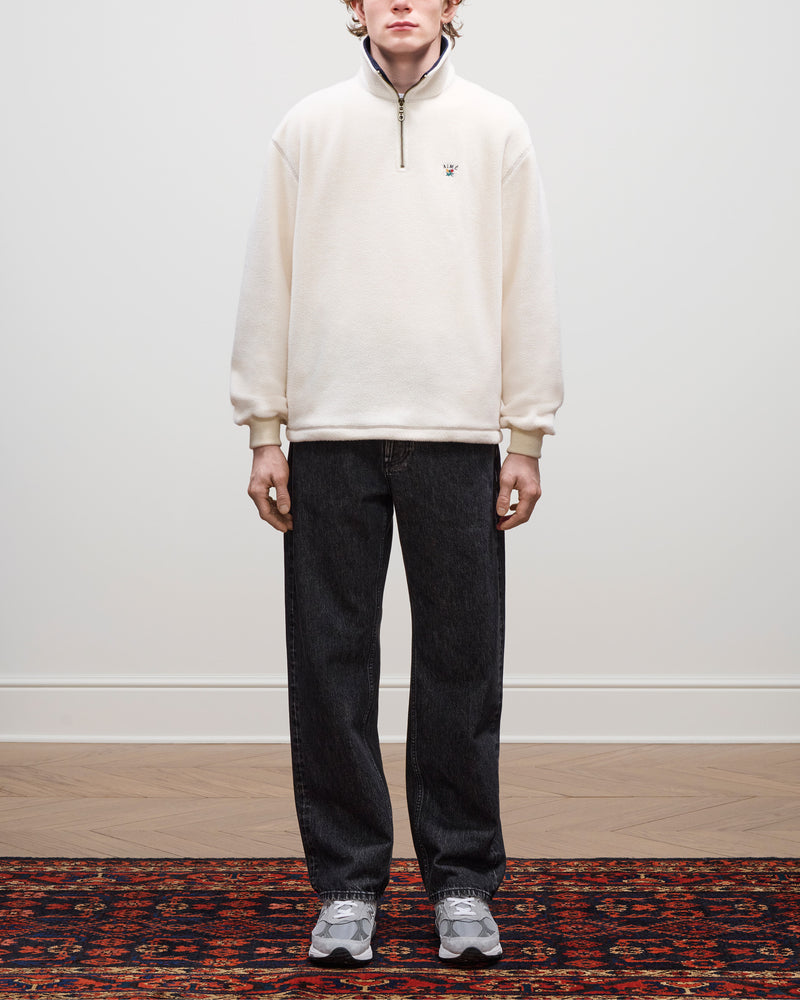 Person standing on a patterned rug, wearing a Crest Quarter-Zip Fleece Pullover, dark jeans, and gray sneakers.