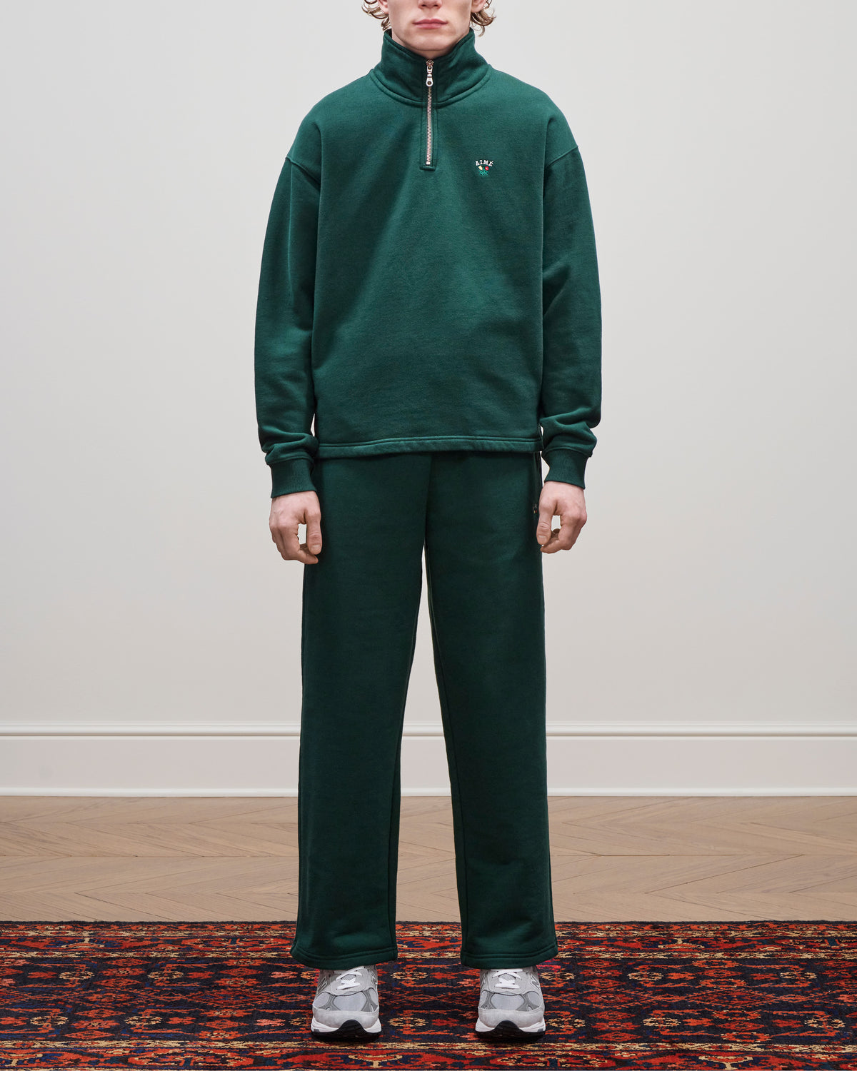 Person wearing the Crest Quarter Zip Pullover, standing on a patterned rug with gray sneakers against a plain background.