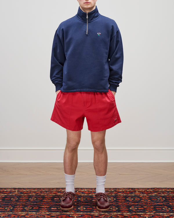 Person wearing a navy Crest Quarter Zip Pullover, red shorts, white socks, and brown loafers on a patterned rug.