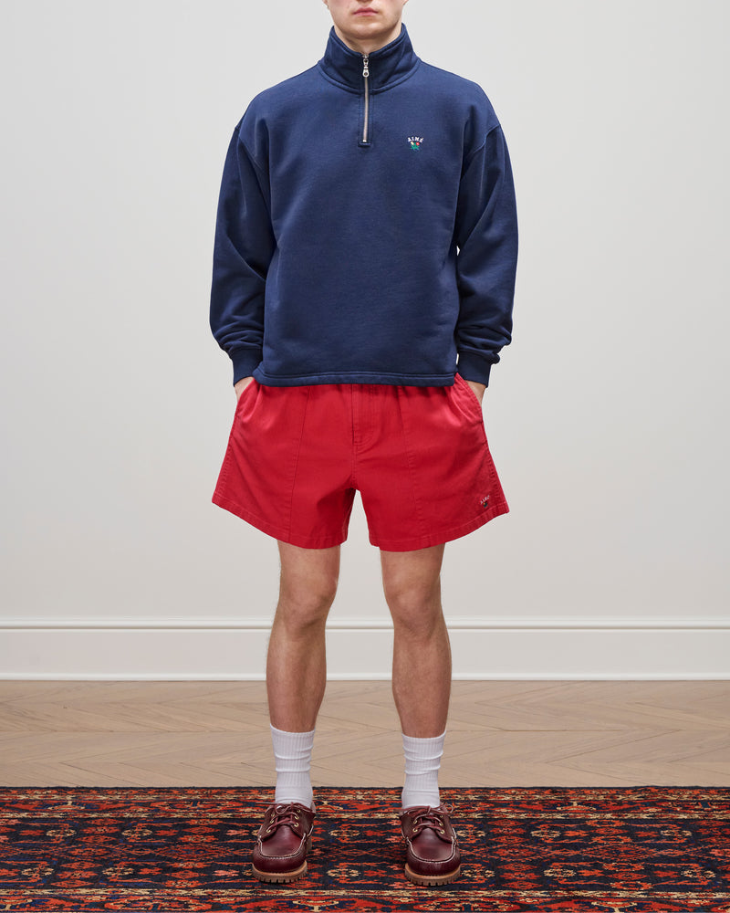 Person wearing a navy Crest Quarter Zip Pullover, red shorts, white socks, and brown loafers on a patterned rug.