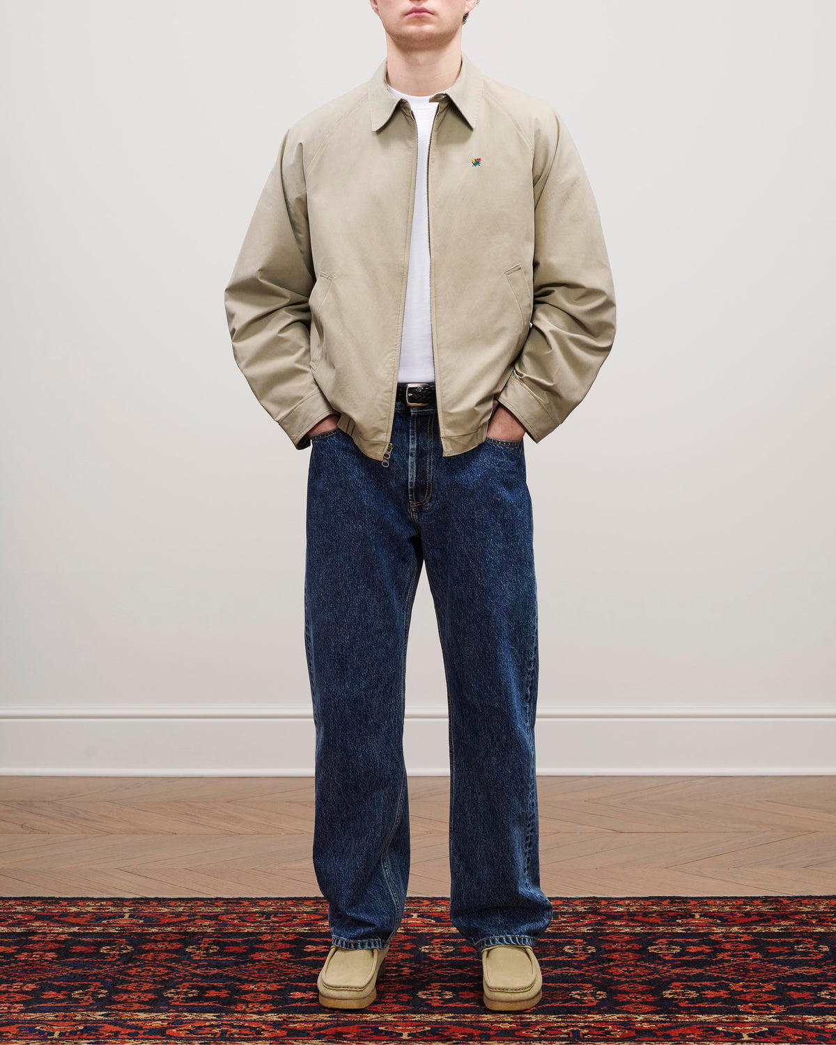 A person in a Crest Casual Jacket, white shirt, blue jeans, and tan shoes stands on a patterned rug.